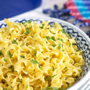 Buttered noodles in a blue and white bowl.