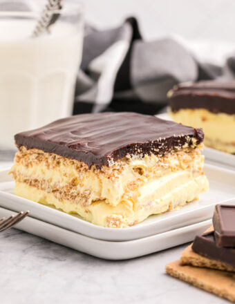 A slice of eclair cake is presented on a white plate in front of a glass of milk.
