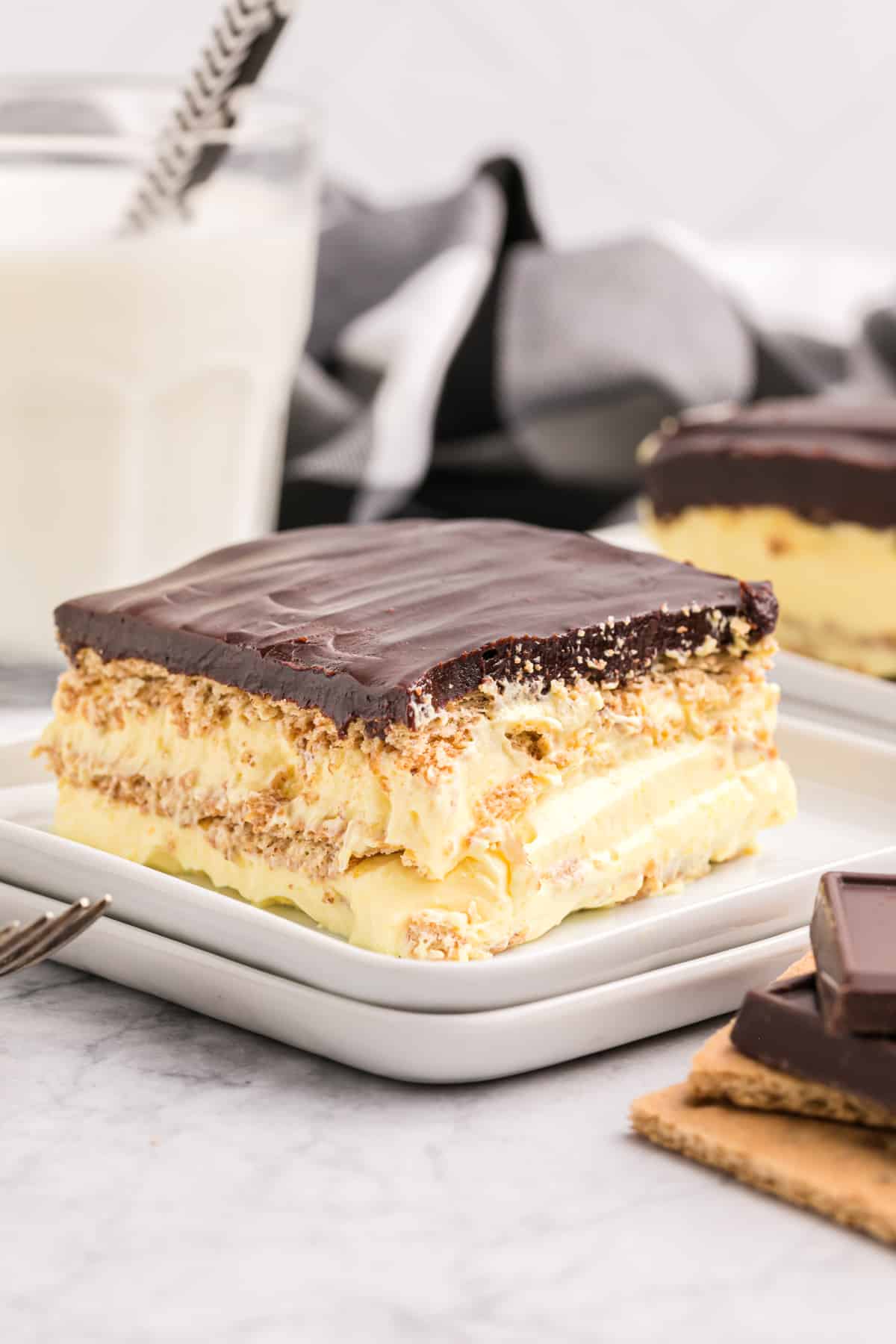 A slice of eclair cake is presented on a white plate in front of a glass of milk.