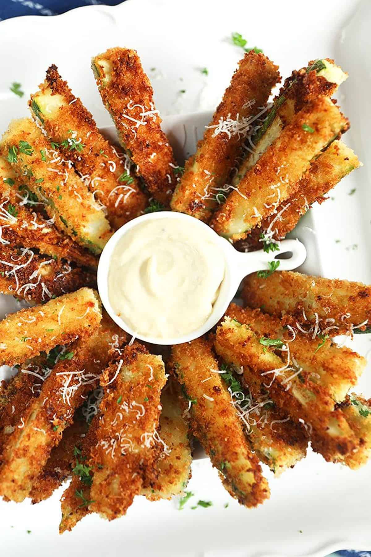 Fried Zucchini on a white platter with a bowl of aioli.