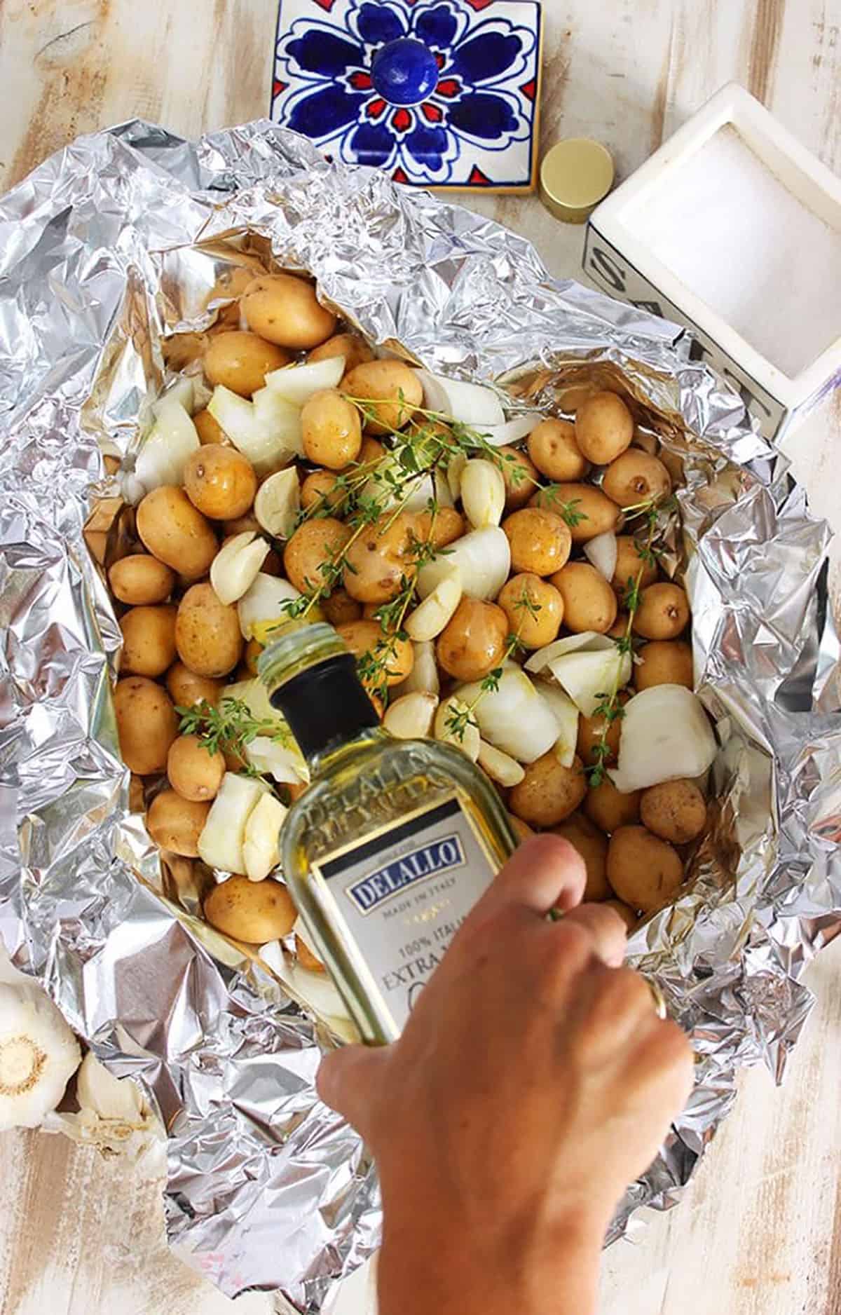 potatoes in a foil packet with a bottle of olive oil being drizzled on top