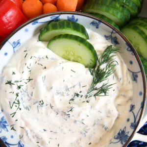 Cucumber slices are placed in a bowl of dill dip.