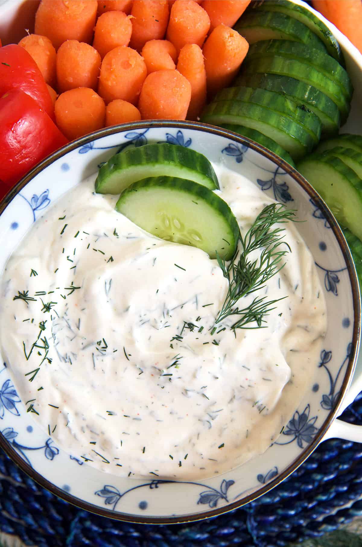 Cucumber slices are placed in a bowl of dill dip.