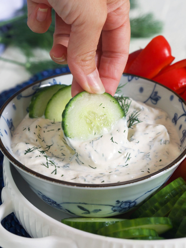 A hand is dipping cucumbers into the dill dip.