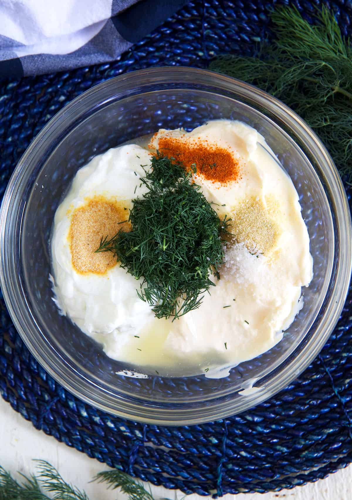 The ingredients for homemade dill dip are placed in a glass bowl and have not yet been mixed.