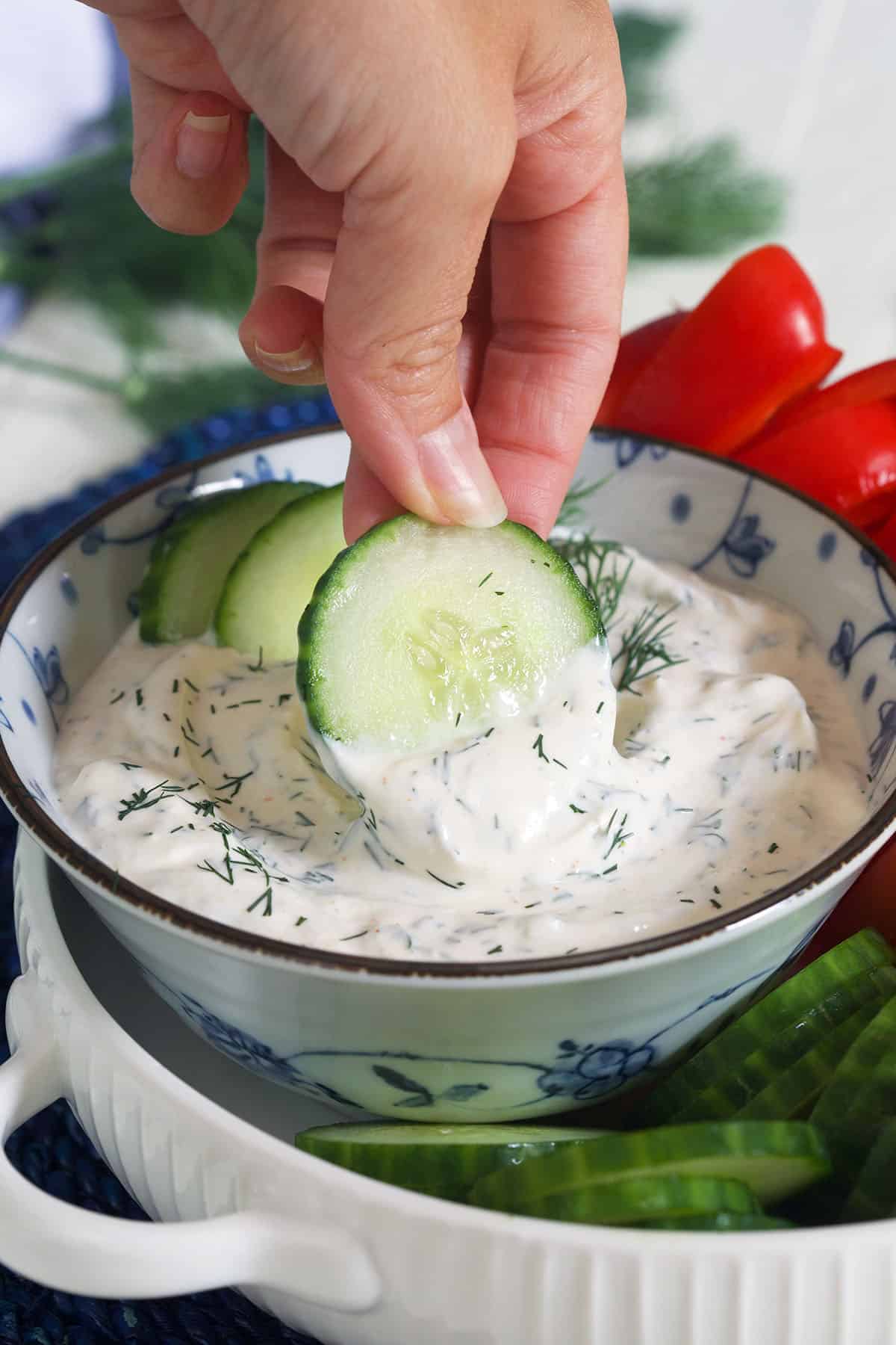 A hand is dipping cucumbers into the dill dip.