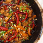 A black skillet is filled with cooked kung pao chicken.