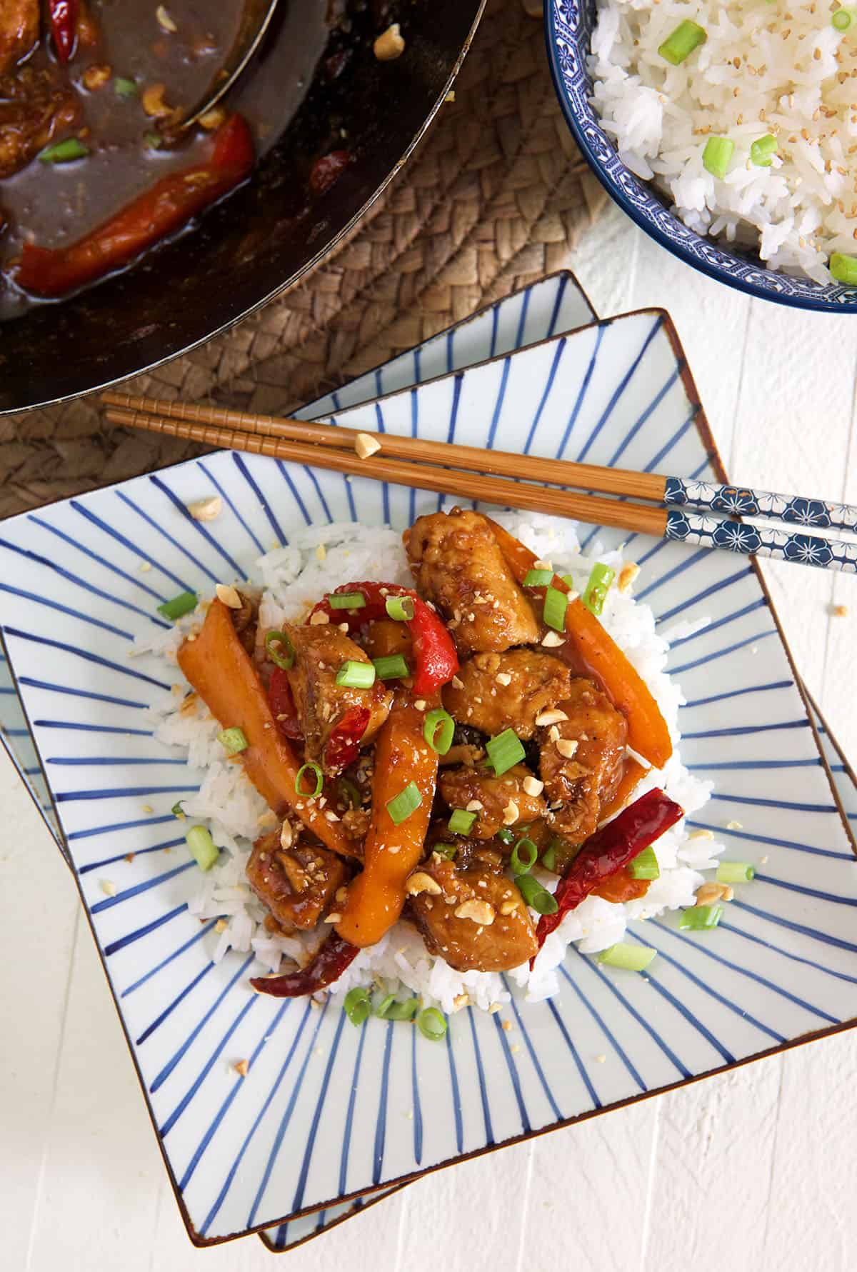 A serving of kung pao chicken is presented with white rice on a striped plate.
