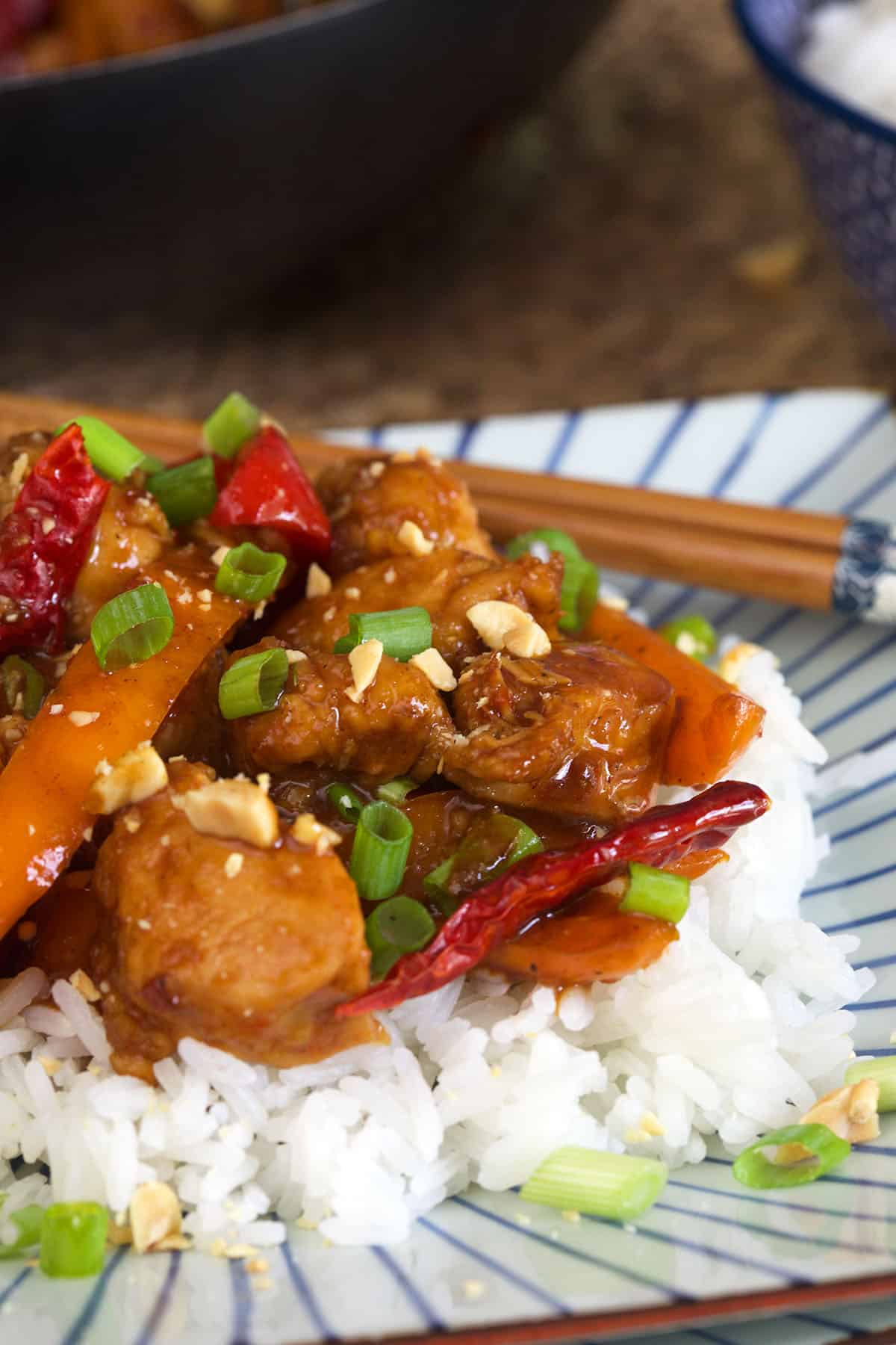 A pile of kung pao chicken is stacked on top of a fluffy serving of white rice.