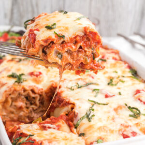 A single lasagna rollup is being lifted from the baking dish.
