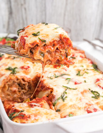A single lasagna rollup is being lifted from the baking dish.