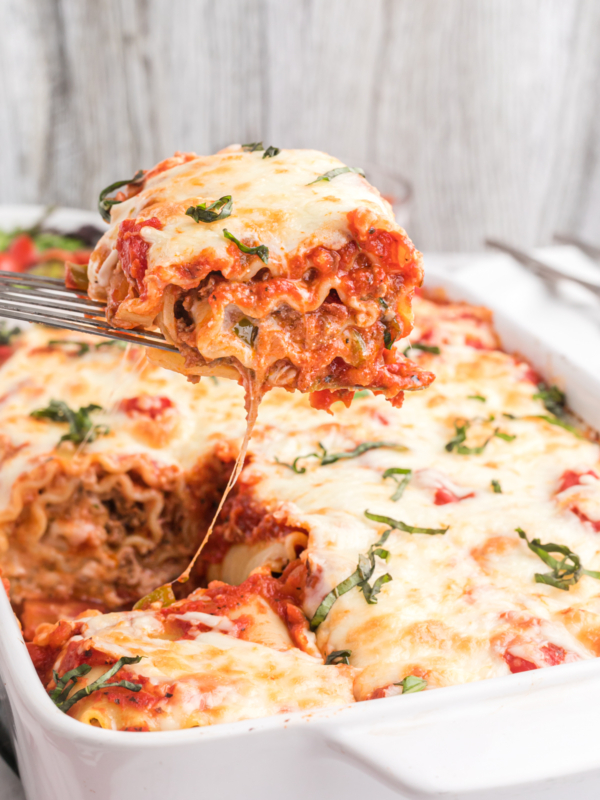 A single lasagna rollup is being lifted from the baking dish.