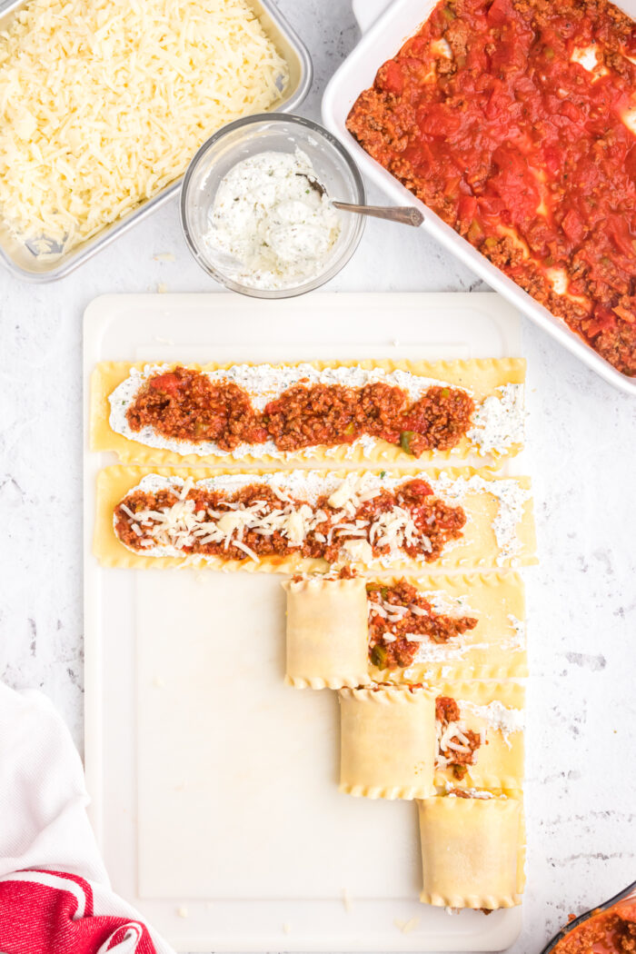 Lasagna rollups are in the process of being rolled on a cutting board.