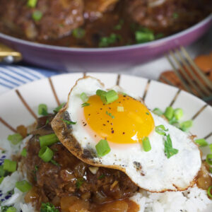 A fried egg is placed on top of a serving of rice and cooked meat with brown sauce.