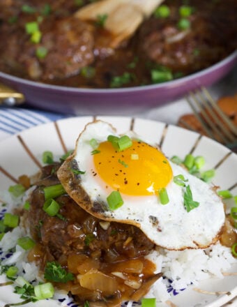 A fried egg is placed on top of a serving of rice and cooked meat with brown sauce.