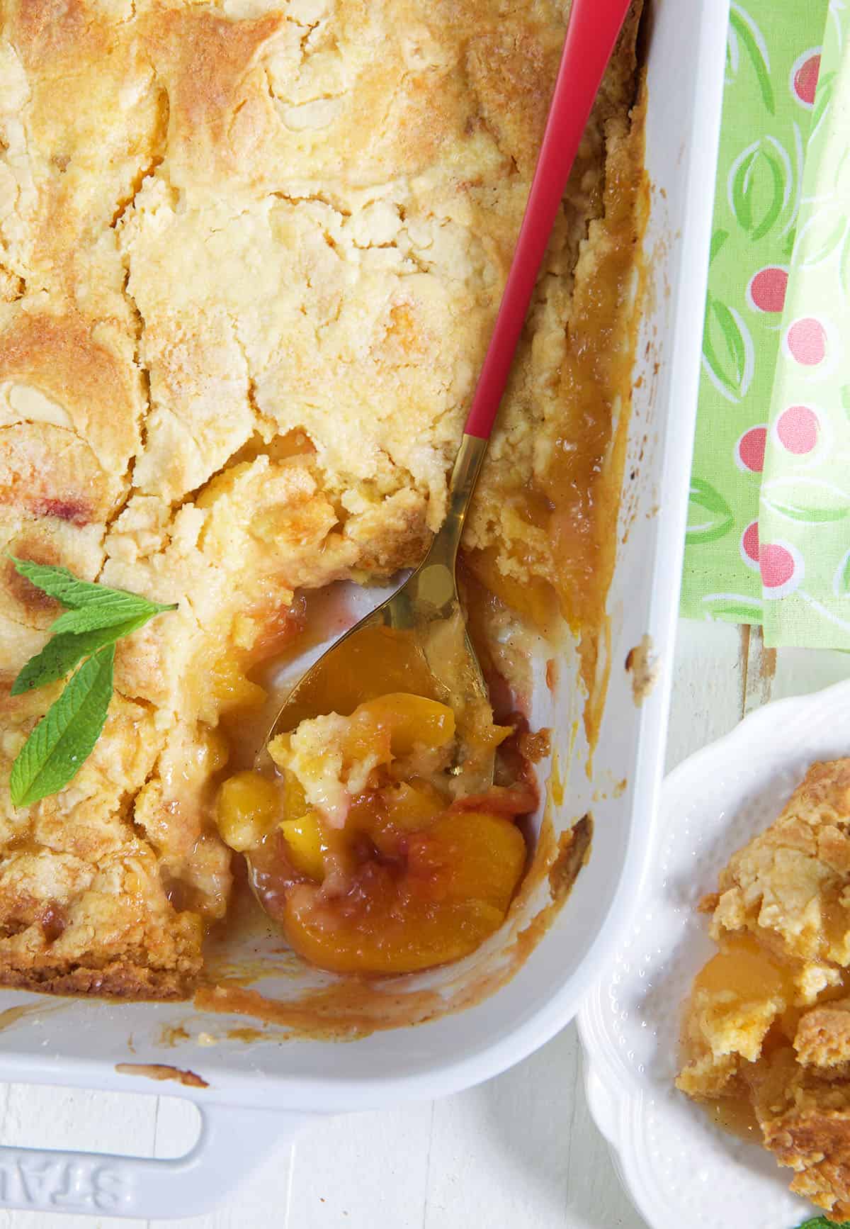 A large spoon is digging into a corner of the peach dump cake.
