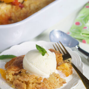 A serving of peach dump cake and vanilla ice cream is placed on a white plate.