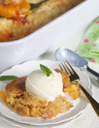 A serving of peach dump cake and vanilla ice cream is placed on a white plate.