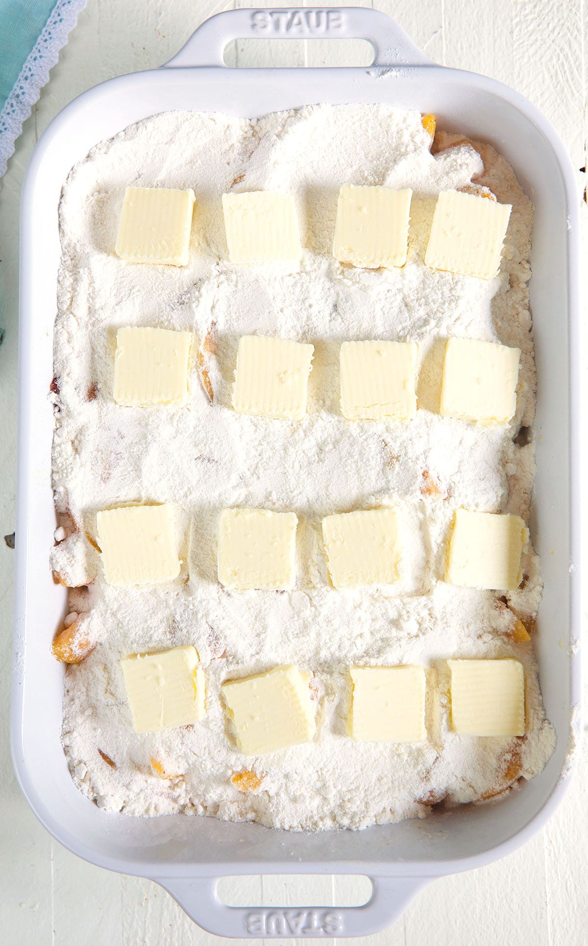 A white baking dish is filled with an unbaked dump cake topped with squares of butter.