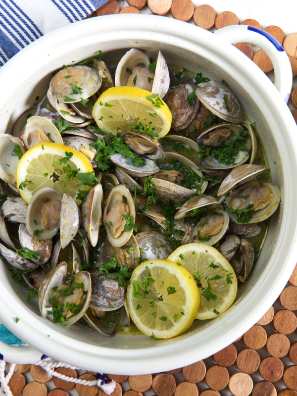 A white pot is filled with cooked clams, herbs, and lemon slices.