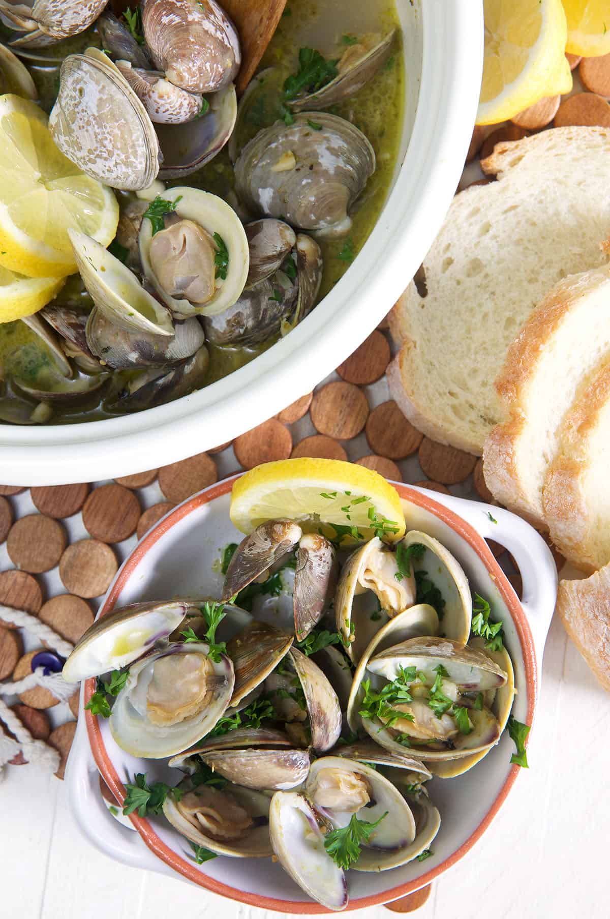 A bowl of steamed clams is placed next to an open pot with more clams. 