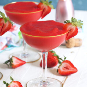Two glasses of strawberry frose are placed on a white countertop next to several sliced strawberies.