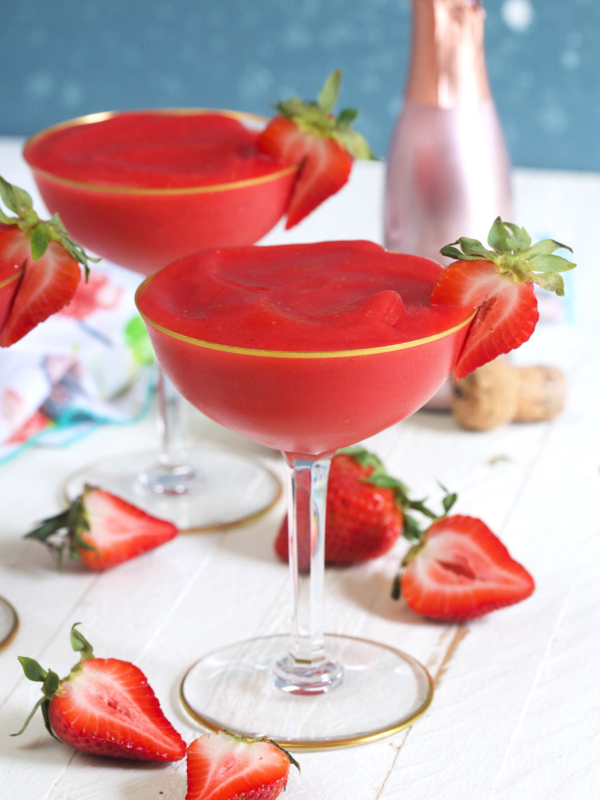 Two glasses of strawberry frose are placed on a white countertop next to several sliced strawberies.
