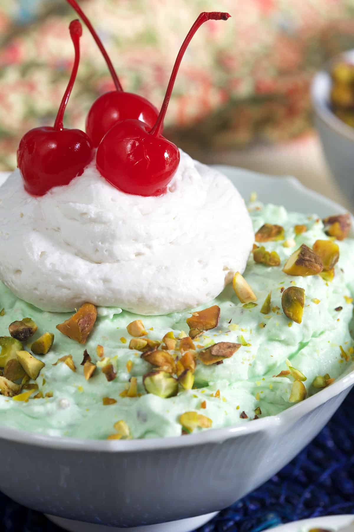 A dollop of whipped cream and three cherries is placed on top of watergate salad.