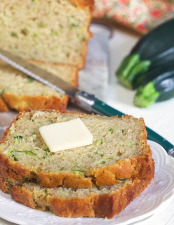 Two slices of zucchini bread are placed on a white plate with a little square of butter on top.