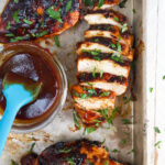 A chicken breast is sliced and presented next to a small bowl of extra BBQ sauce.