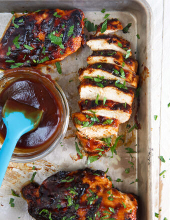 A chicken breast is sliced and presented next to a small bowl of extra BBQ sauce.