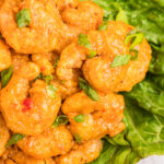 A plate of lettuce and bang bang shrimp is garnished with chopped green onions.