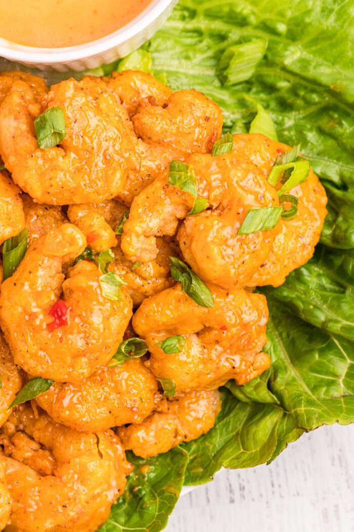 A plate of lettuce and bang bang shrimp is garnished with chopped green onions.