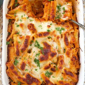 Overhead shot of baked rigatoni bolognese in a white baking dish on a blue background.