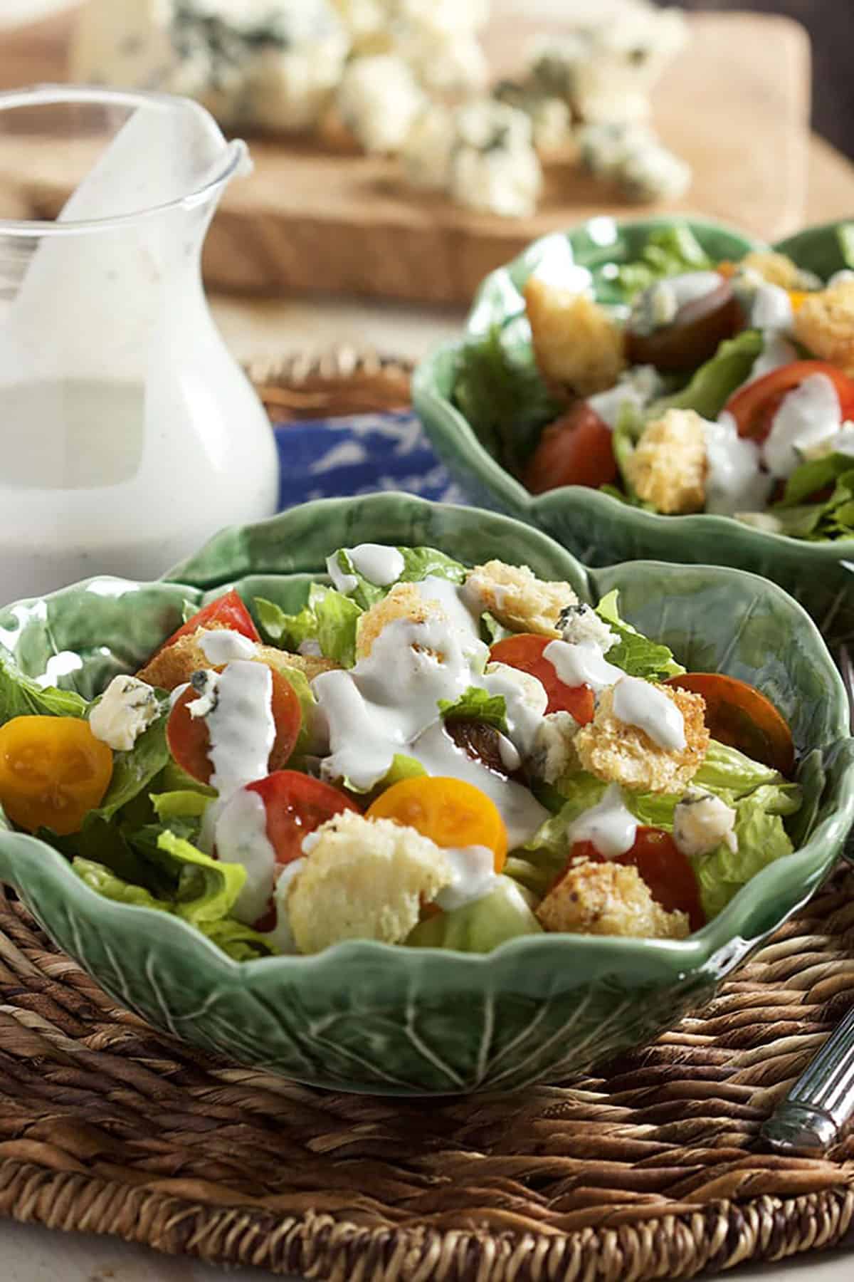 Salad dressed with Blue Cheese Dressing with a small glass pitcher of dressing in the background