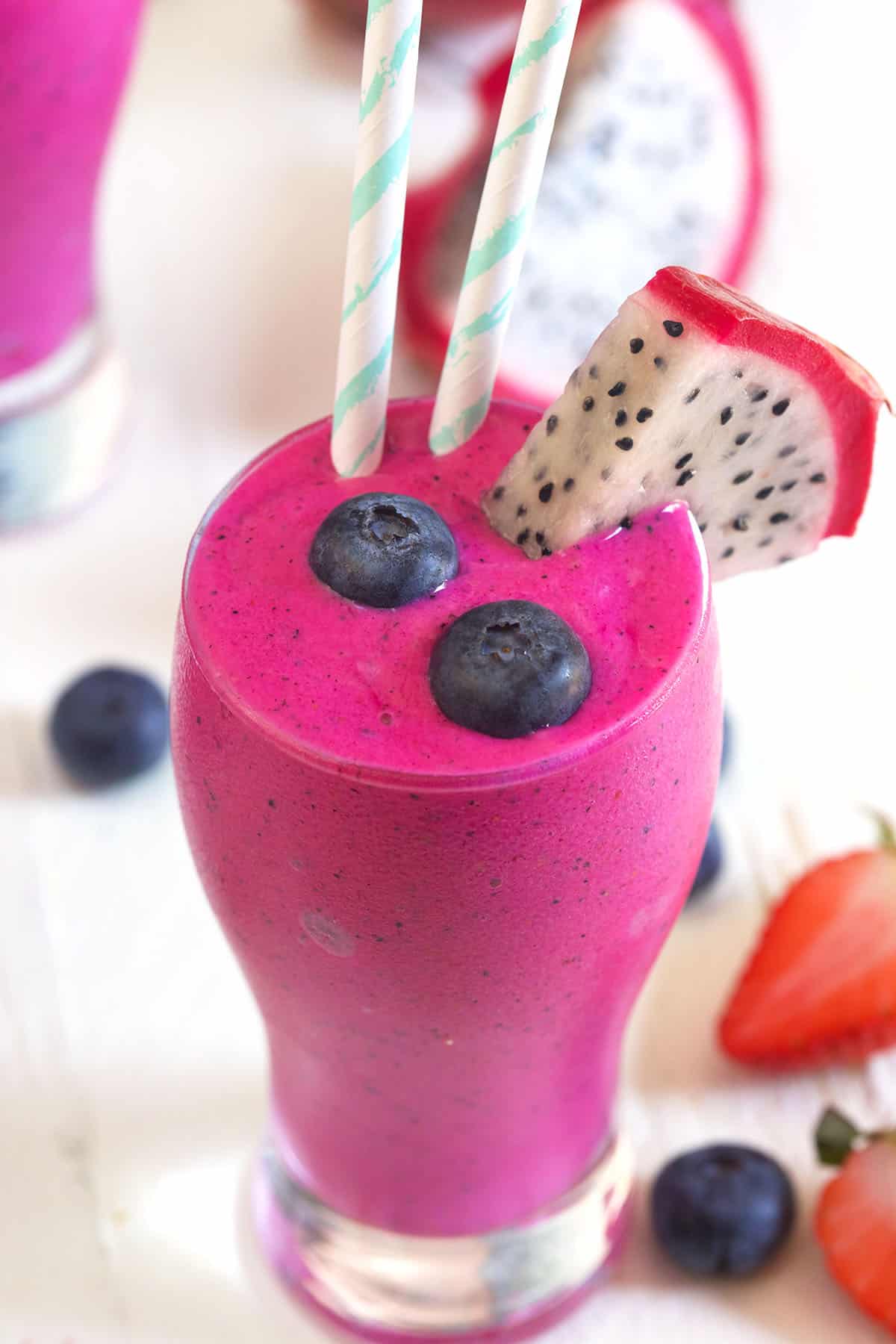 A pitaya smoothie is garnished with fresh fruits and two straws.