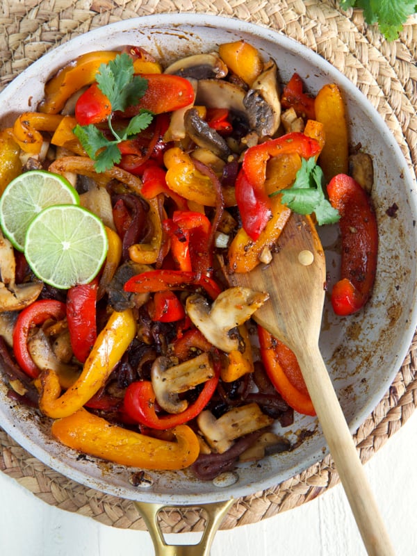 A wooden spoon is mixing up veggies in a pan.