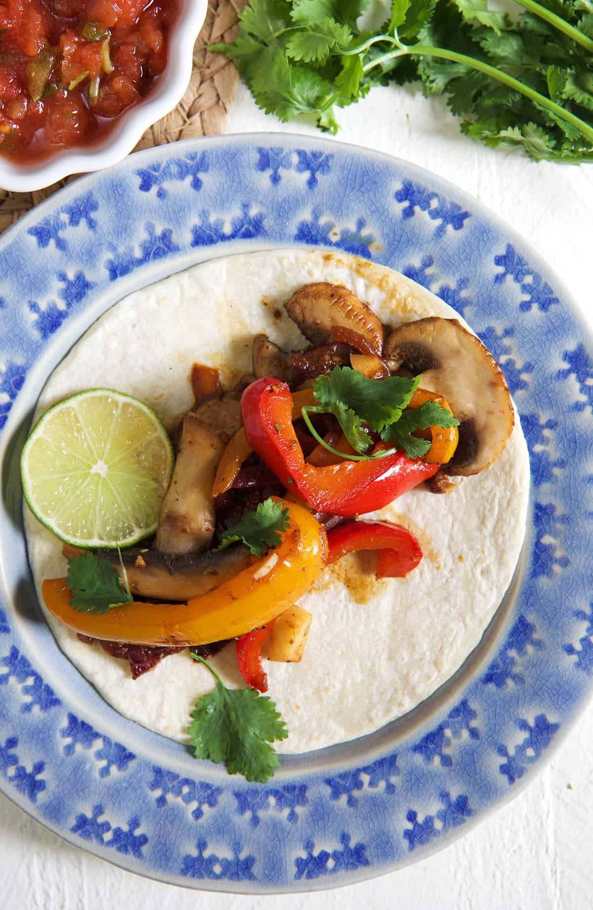 An open tortilla is filled with fajita veggies and a lime wedge.