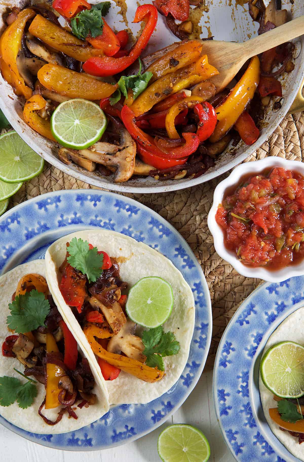 Peppers are being cooked in a pan next to a plate with two fajitas on it.