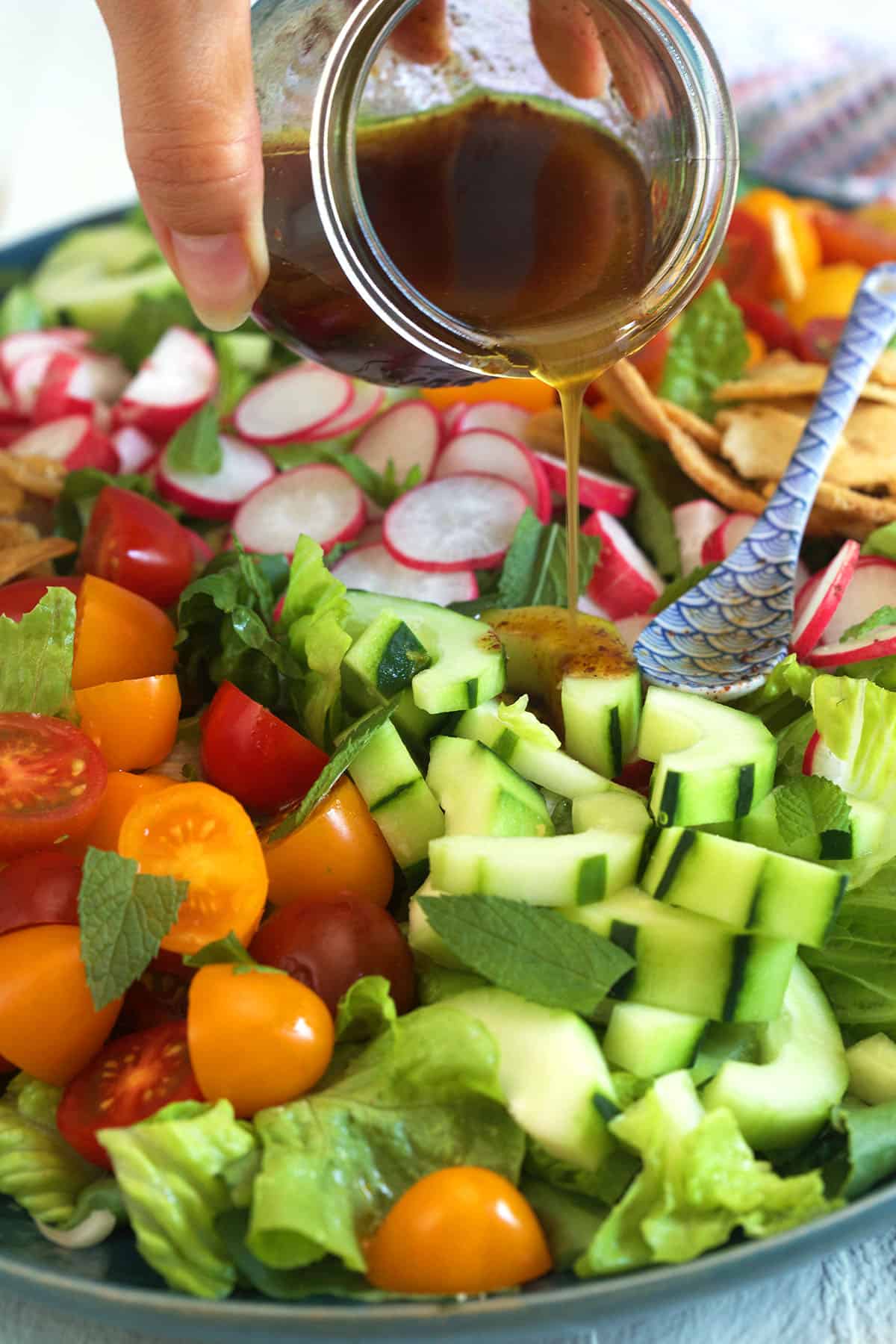 Homemade dressing is being drizzled over a fattoush salad.