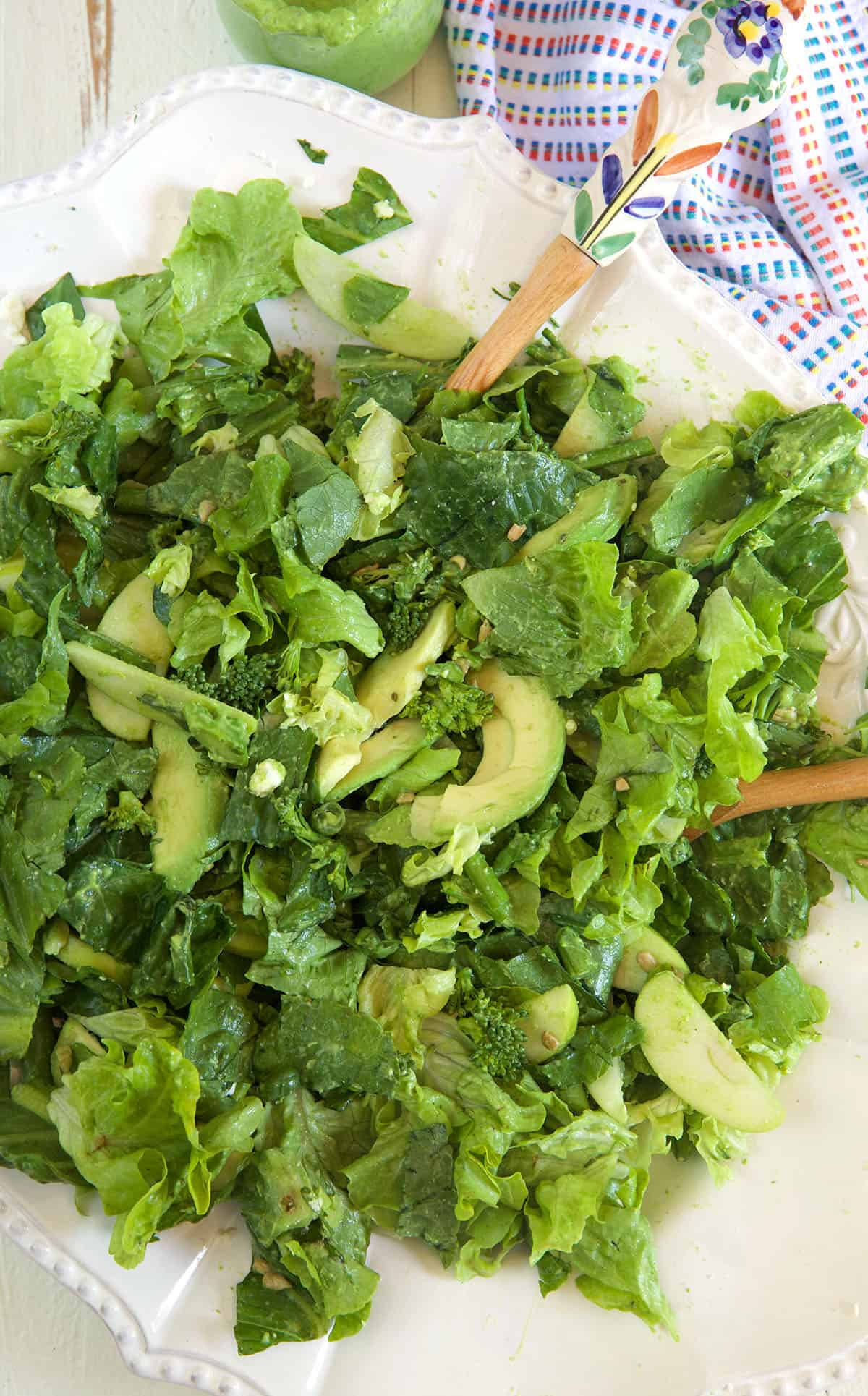A tossed green goddess salad is ready to be served from a white bowl.