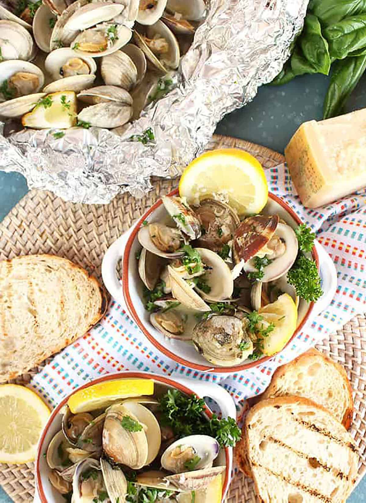 Overhead shot of grilled clams with parmesan, basil and grilled bread on a blue background.