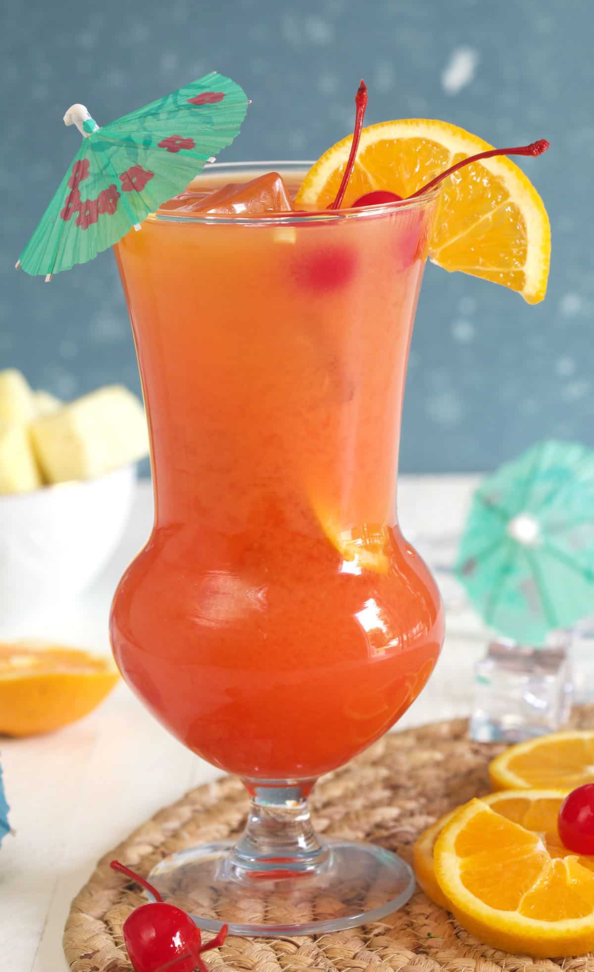 A hurricane is topped with cherries, an orange slice, and an umbrella.