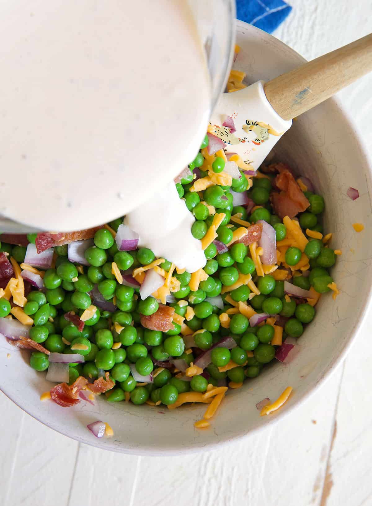 Dressing is being poured into a bowl of tossed pea salad.