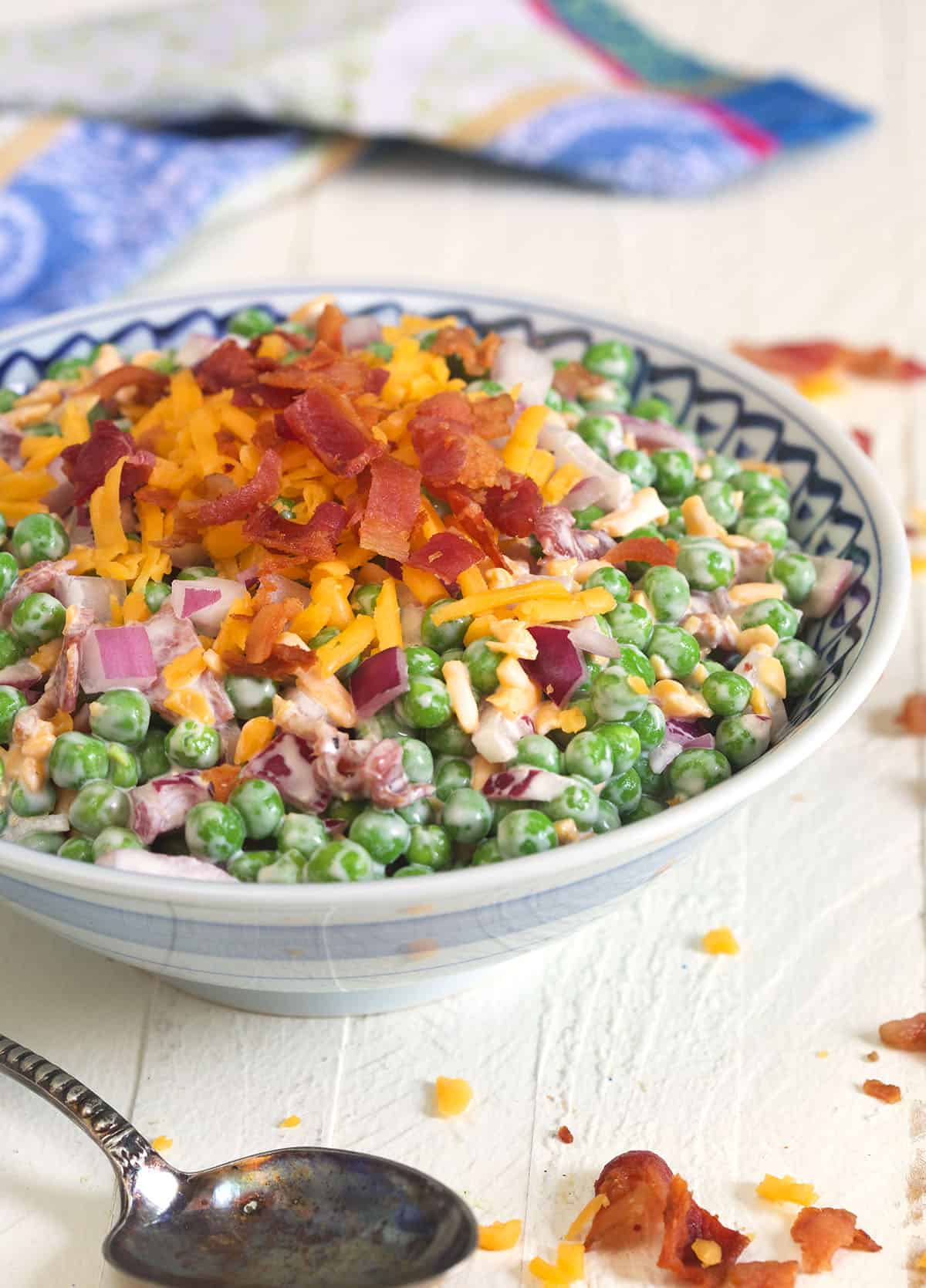 A bowl of pea salad is topped with cheese, bacon, and onions.