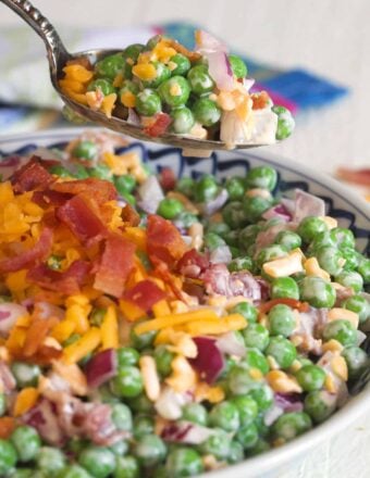 A spoon is lifting a small portion of pea salad from the bowl.