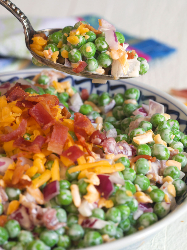 A spoon is lifting a small portion of pea salad from the bowl.