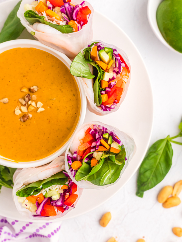 Several halved spring rolls are placed around a bowl of peanut sauce.