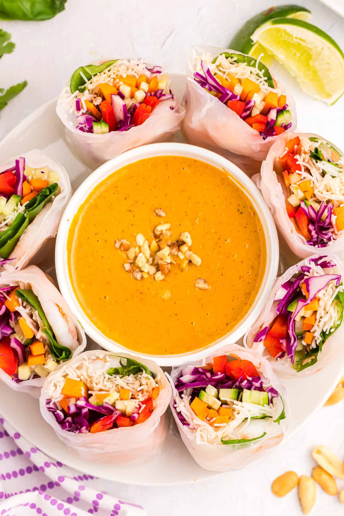 A large serving of peanut sauce is presented in the middle of severeal halved summer rolls.