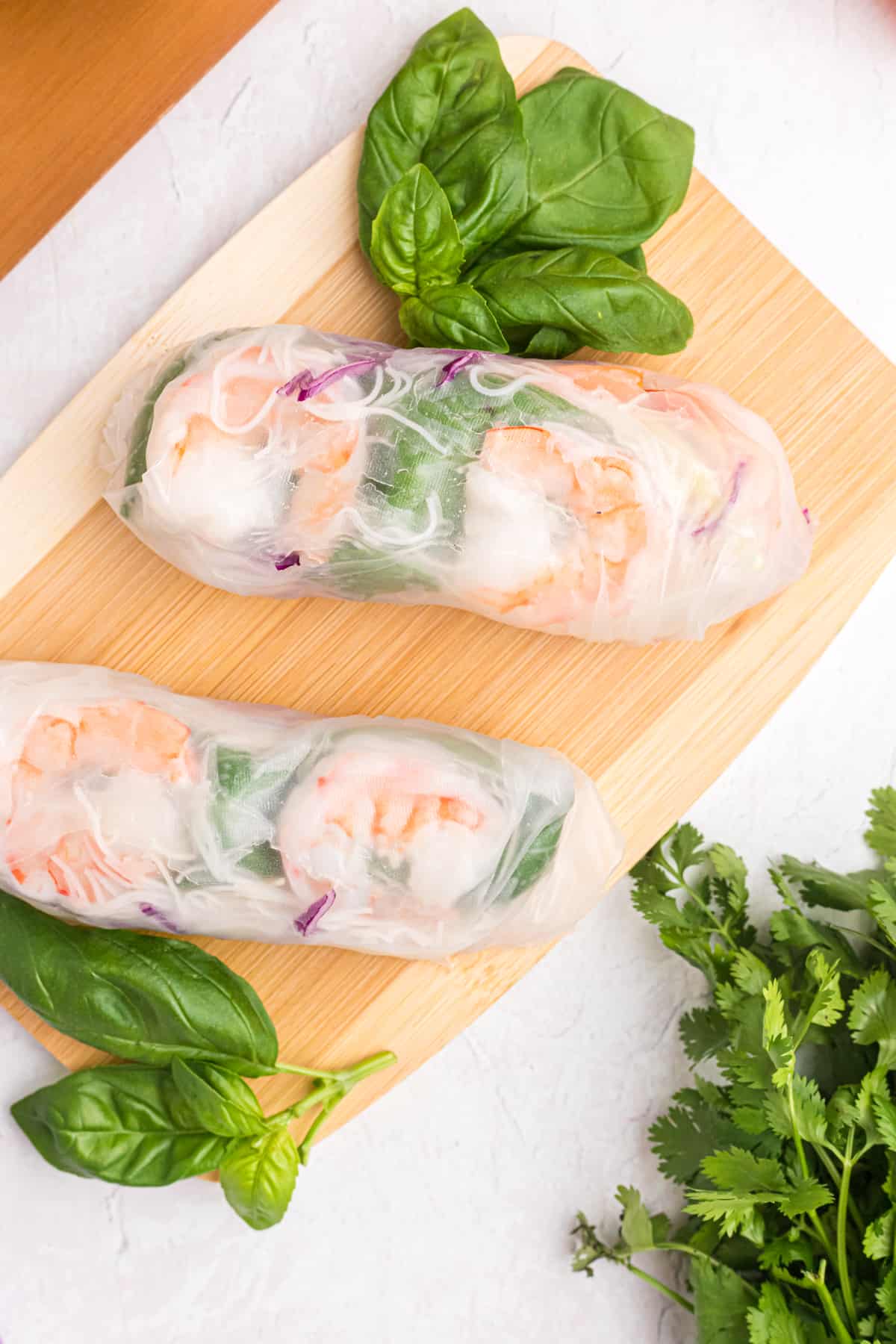 Two summer rolls are placed on a wooden cutting board. 
